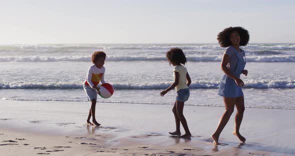 African american mother and her children playing with a ball on the beach