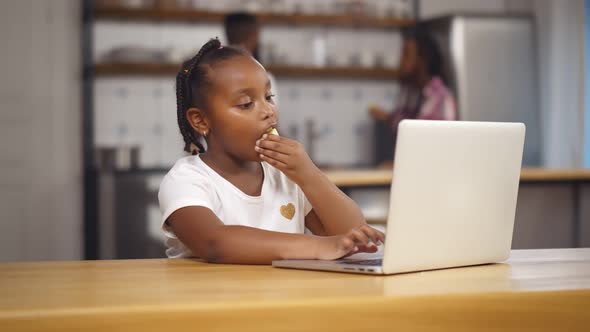 African Schoolgirl Eating Apple and Learning at Home with Laptop