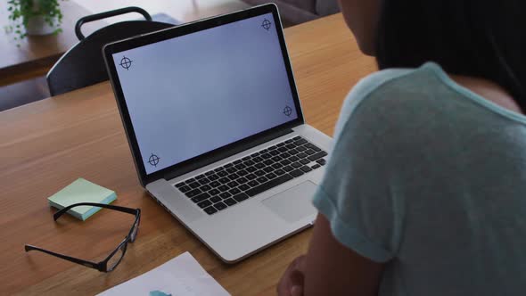 Mixed race gender fluid person sitting at desk working from home using a laptop