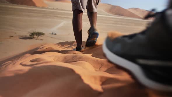 Two people walking down the famous Dune 45 in Namibia. Sand is stirred up and the shoes sink into th