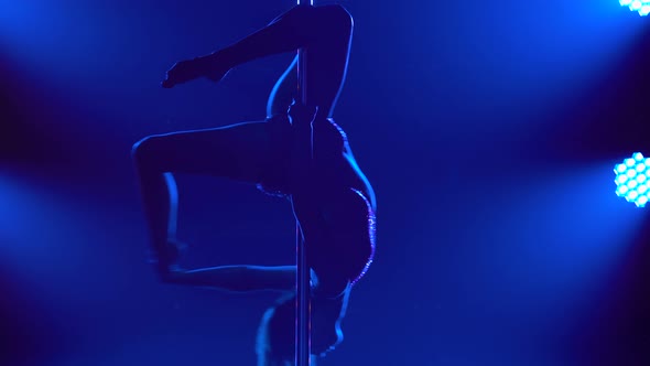 The Dancer Spins Around the Pole Upside Down in a Dark Studio