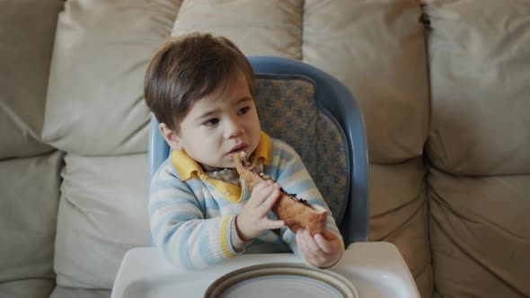 Asian Baby Eats Pizza Sits on the Baby's Feeding Table