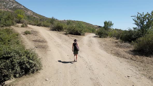 Girl Traveler Walks Alone in a Hat on the Road in the Mountains