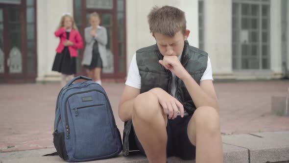 Portrait of Schoolboy Coughing As Blurred Classmates Showing No Gesture at the Background