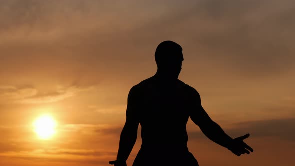 Silhouette of a Strong Man Does a Breathing Exercise Alone at Sunset, Meditating on Sunset