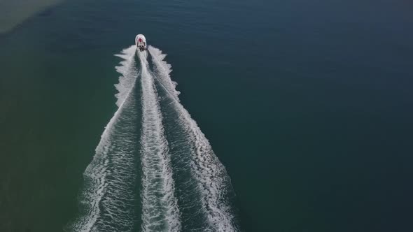 Chase aerial as white speed boat splashes wake in shallow green lagoon