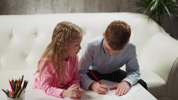 Little Girl Looks at Brother Drawing Patterns on Paper