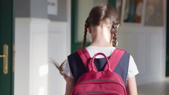 Follow Shot of Preteen Girl with Braids and Backpack Walking in Empty School Corridor