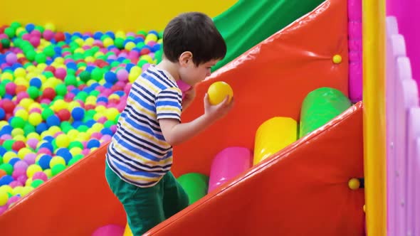 The Boy Climbs the Slide on a Colored Soft Staircase From the Pool with Soft Balls