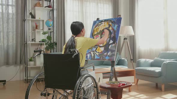 Hind View Of Asian Artist Girl In Wheelchair Holding Paintbrush And Painting A Girl's Face