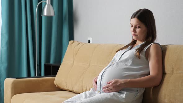 Young Pregnant Woman Stroking Belly While Sitting on the Sofa