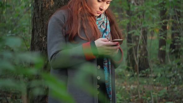 Girl with Stands in the Forest in the Autumn Forest and Writes Sms