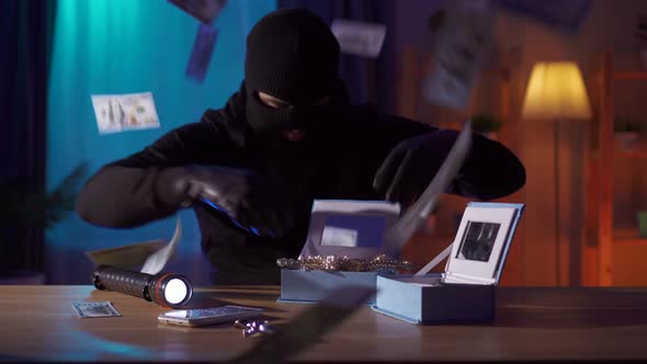 Funny Robber in a Balaclava Finds Jewelry on the Table and Tries Them on Himself