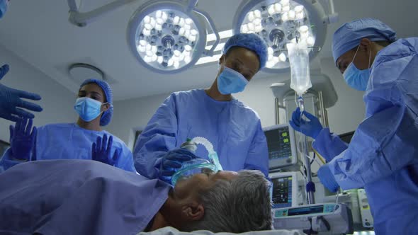 Mixed race surgeons wearing protective clothing putting patient to sleep in operating theatre