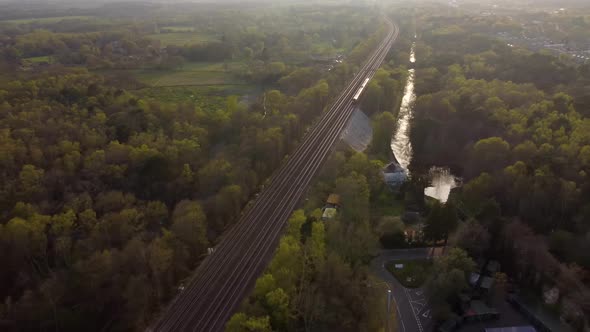 Beautiful aerial view of train travelling at sunset with forest and fields