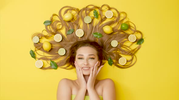 beautiful girl lying on colored background with citrus fruits fruits on long hair, female flirting