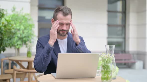 Man with Headache Working on Laptop Sitting in Outdoor Cafe