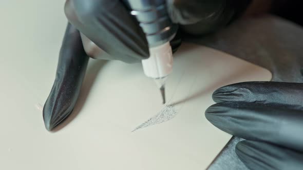 Gloved Hands Draw an Eyebrow on a Silicone Mat with a Tattoo Machine