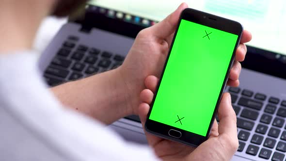 A Black Smartphone with Green Screen for Chroma Key Compositing the Hands of a Man on Laptop