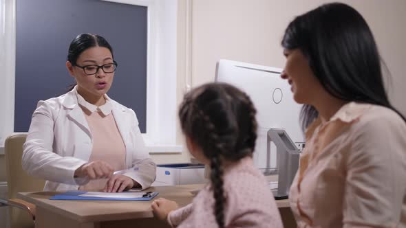 Friendly Asian Pediatrician Writing Prescription