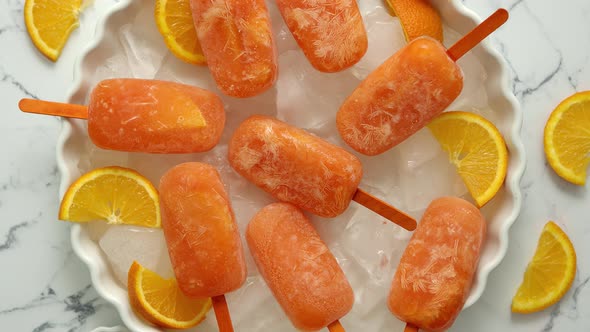 Homemade, Juicy, Orange Popsicles, Placed on a White Plate with Ice Cubes