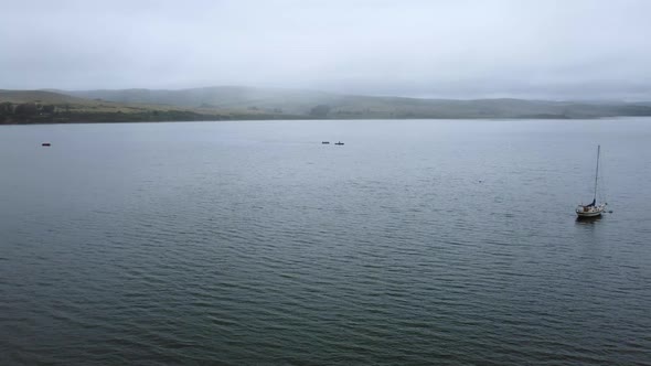 Drone Flying Over Quiet Blue Water Towards Foggy Mountain, California