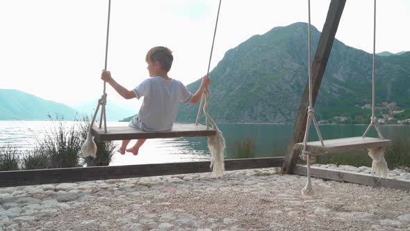 A Girl and a Boy Swing on a Swing Near the Sea with a Beautiful View of the Bay and Mountains