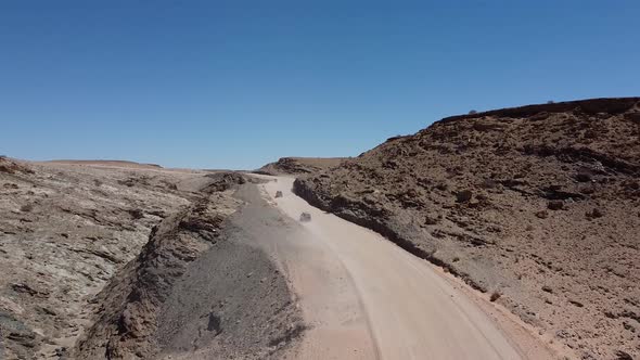 Drone footage of three cars driving on a dusty road in the desert, Namibia