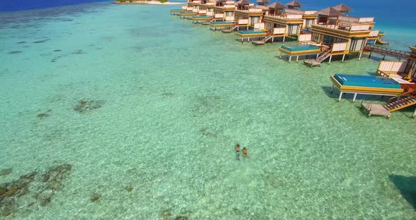 Aerial drone view of a man and woman couple with seascooters snorkeling near overwater bungalows.