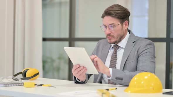 Middle Aged Engineer using Tablet while Sitting in Office