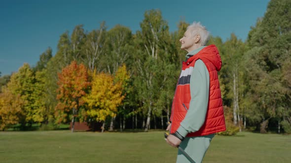 Aged Woman Doing Nordic Walking in Sunny Fall Park By Herself Side View