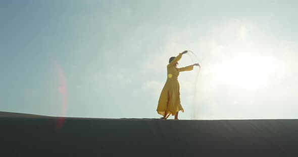 Stylish Woman in Yellow Dress Walking on Top of Sand Dune in Slow Motion