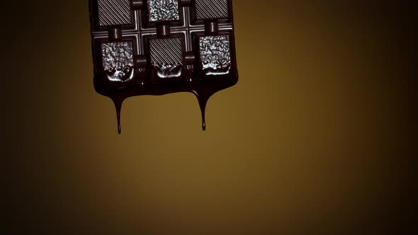Slow Motion of Chocolate Bar with Melted Dark Chocolate Dripping Flowing Over Brown Background