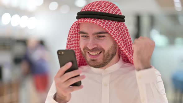 Portrait of Excited Arab Businessman Celebrating Success on Smartphone 