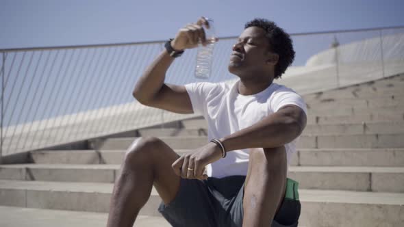 Smiling Sporty Young Man Sitting on Stairs and Drinking Water