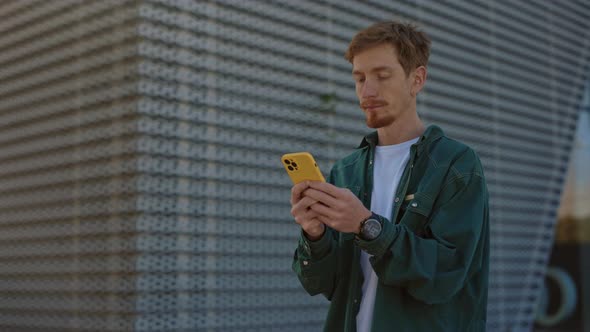 Portrait Handsome Caucasian Guy in Casual Wear Standing on Street with Modern Smartphone in Hands