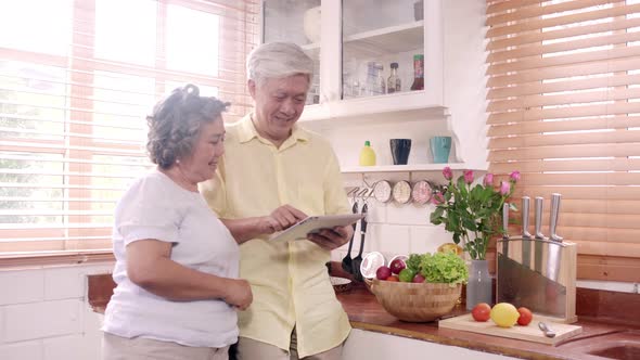 Asian elderly couple using tablet prepare ingredient for making food in the kitche.