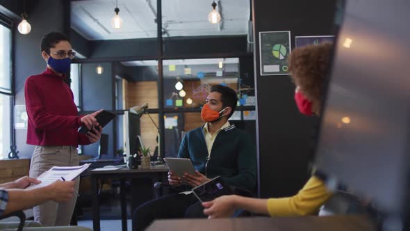 Diverse colleagues wearing face masks discussing together at modern office