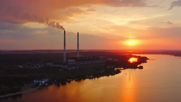 Silhouette of a chemical plant near the river. Industrial factory releases smoke at beautiful sunset