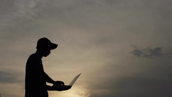 Silhouette of happy young man with cap holding laptop