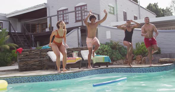 Group of happy diverse female and male friends jumping into swimming pool at pool party