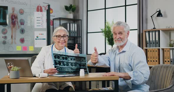 Woman-Doctor in Glasses with X-ray Scan Posing on Camera together with Positive Mature Bearded man