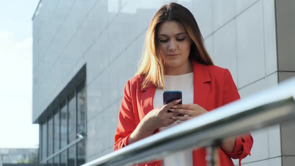 Business Woman in a Red Jacket Reads a Message in a Smartphone
