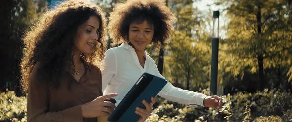 Video of businesswomen walking and discussing with digital tablet outdoors.