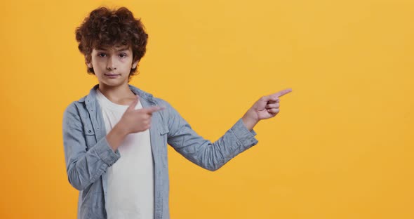 Cool Offer. Little Boy Showing Aside with Both Hands, Pointing at Copy Space , Orange Background