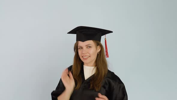 A Young Caucasian Female Student in a Black Robe Touches a Square Hat