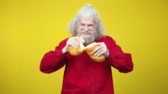 Portrait of Senior Bearded Caucasian Man Breaking Bread Loaf and Eating Tasty Crusty Bakery