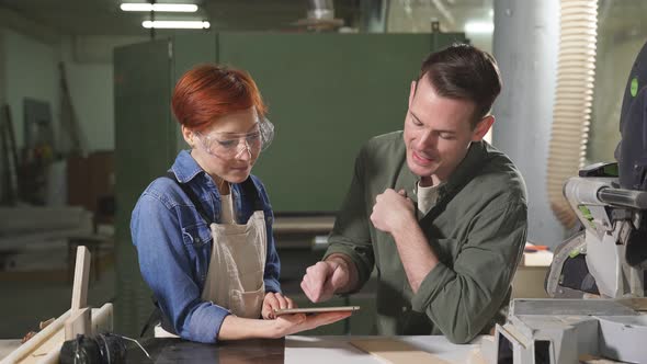 Young Caucasian Man and Woman Joiners Using Digital Tablet While Working in Workshop