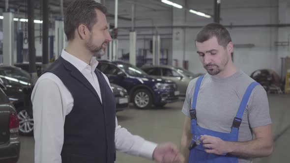 Side View of Handsome Adult Caucasian Man Giving Car Keys To Auto Mechanic and Shaking His Hand