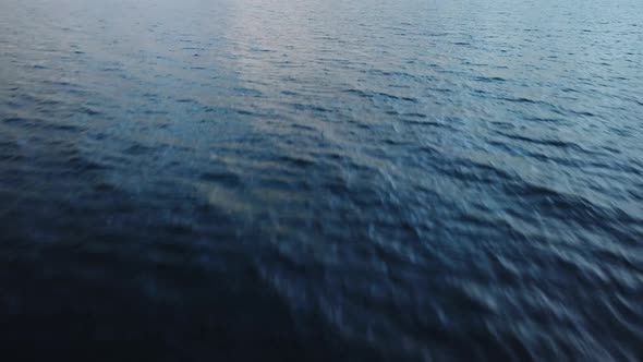 Drone flying fast above lake close to the dark blue water surface. Rising aerial